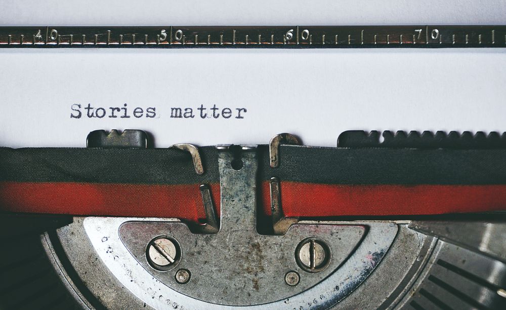 Mesin tik retro dengan kertas bertuliskan Stories Matter, melambangkan prinsip penulisan redaksi Jagoan303